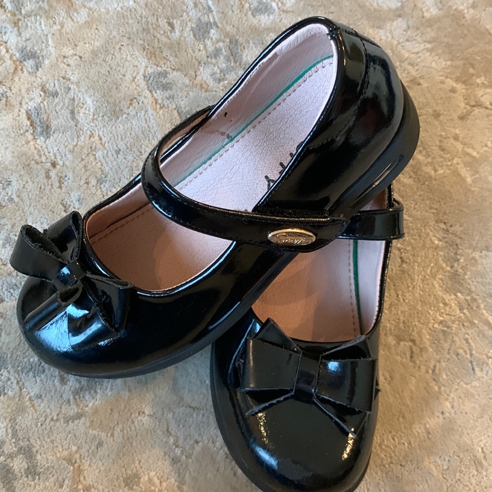 Patent leather black Velcro girls shoes with a bow.